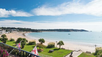 Vista costera con playa, una bandera y un área verde con una estatua.