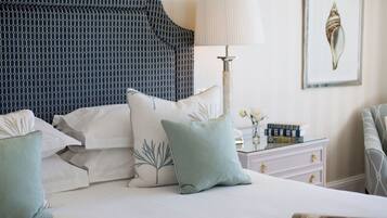 Una cama bien hecha con almohadas, una mesita de noche con libros y una lámpara, y un cuadro en la pared.