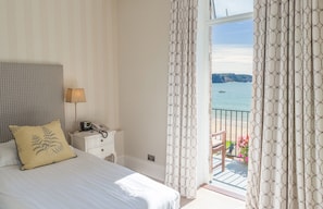 Habitación de hotel con cama, mesita de noche con lámpara, teléfono y vista al mar a través de cortinas.
