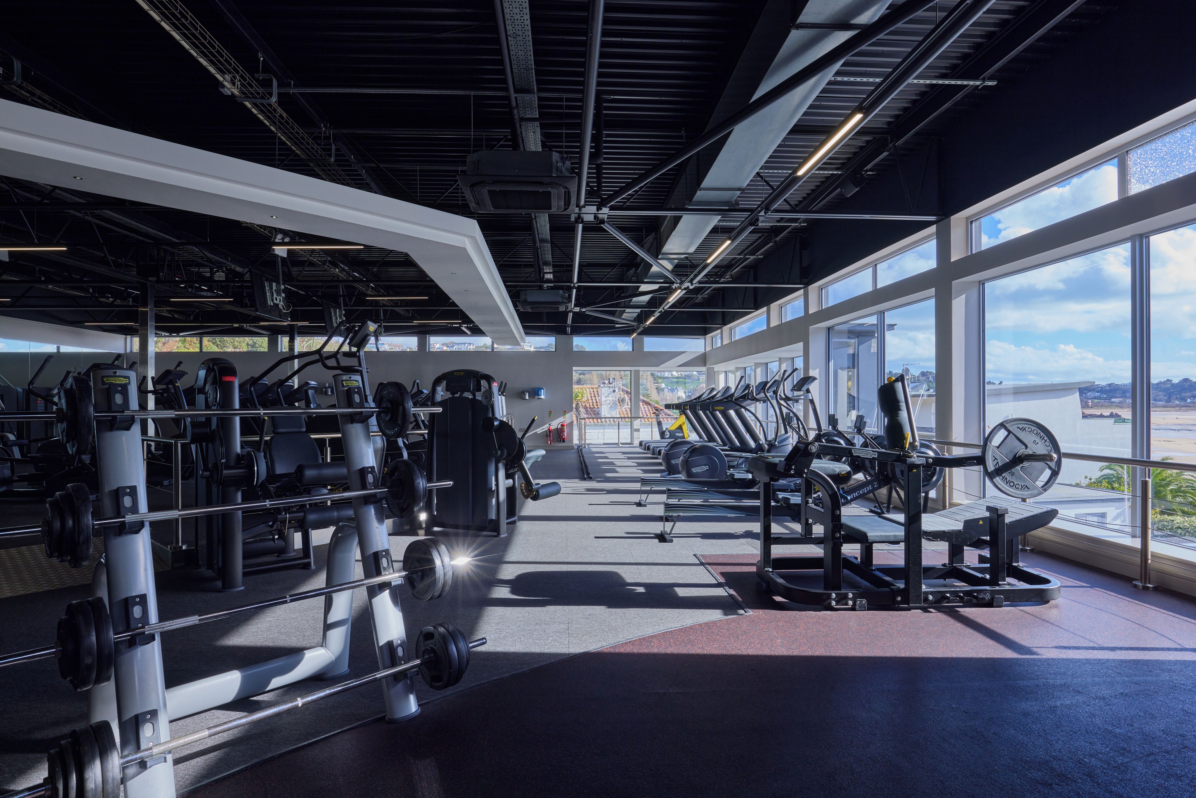 A gym with various exercise equipment, large windows, and a view of the outside.