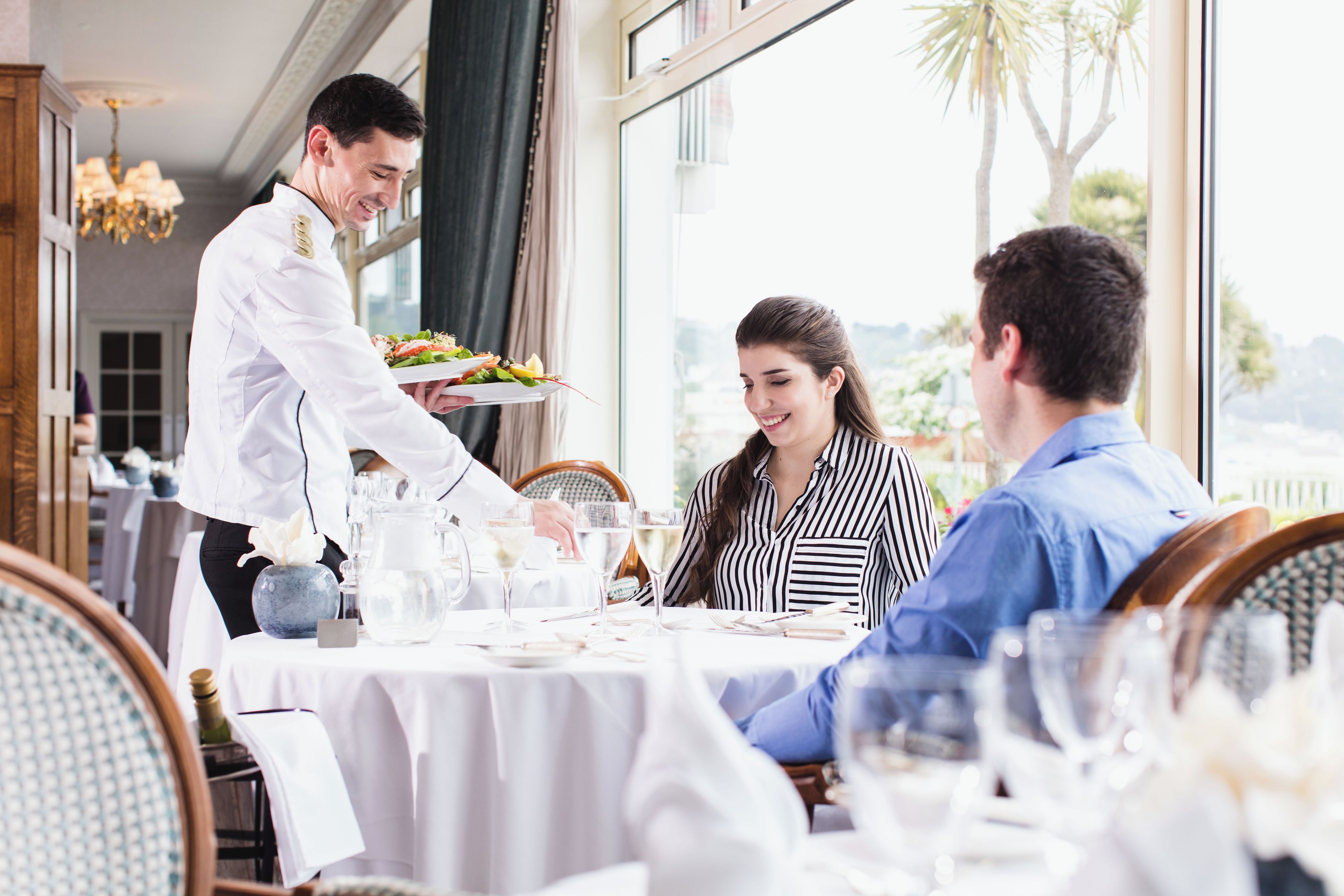 Un restaurante con un camarero sirviendo comida a los clientes en una mesa.