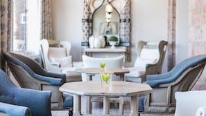 Un rincón acogedor con sillones tapizados y una mesa redonda, un espejo decorativo y una planta pequeña en la mesa.