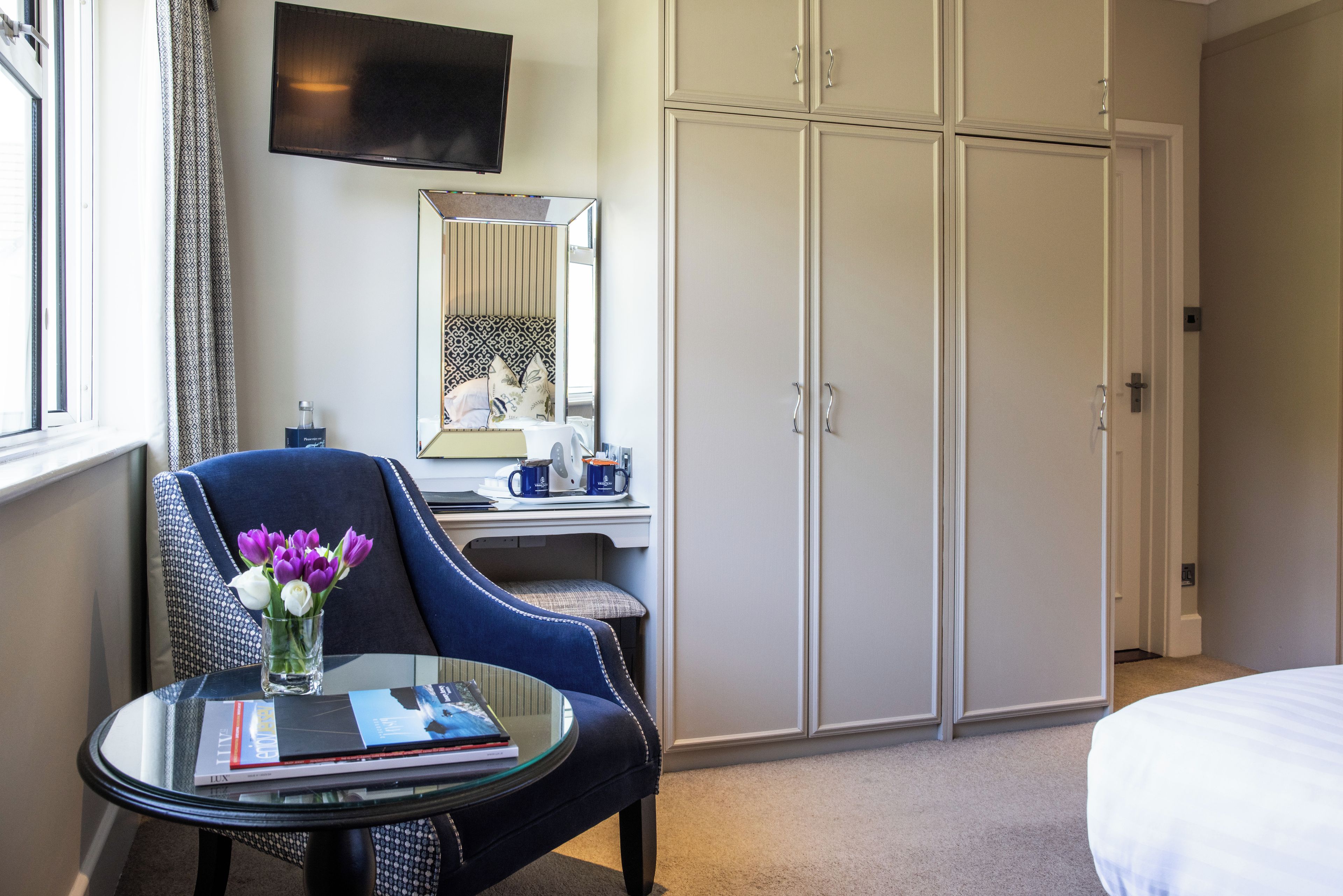 A hotel room with a bed, a desk with a chair, a television, and a wardrobe.
