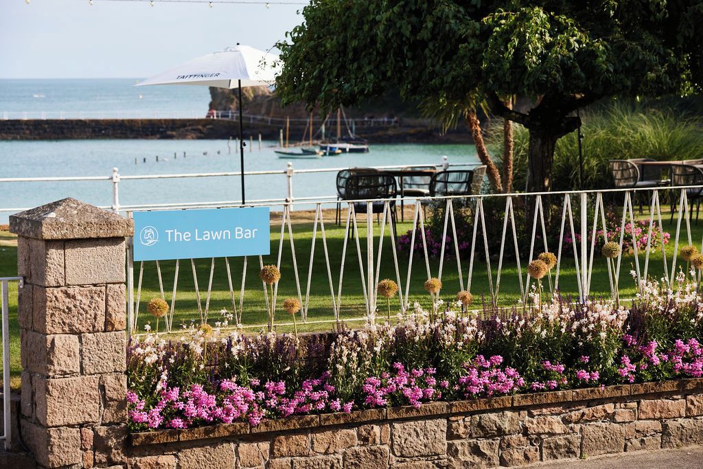 A sign for 'The Lawn Bar' with a view of a waterfront and a grassy area with a fence.