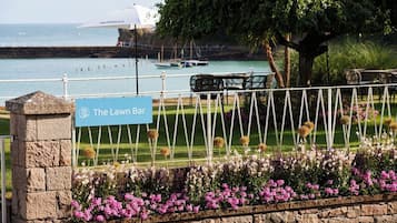 A sign for 'The Lawn Bar' with a view of a waterfront and a grassy area with a fence.