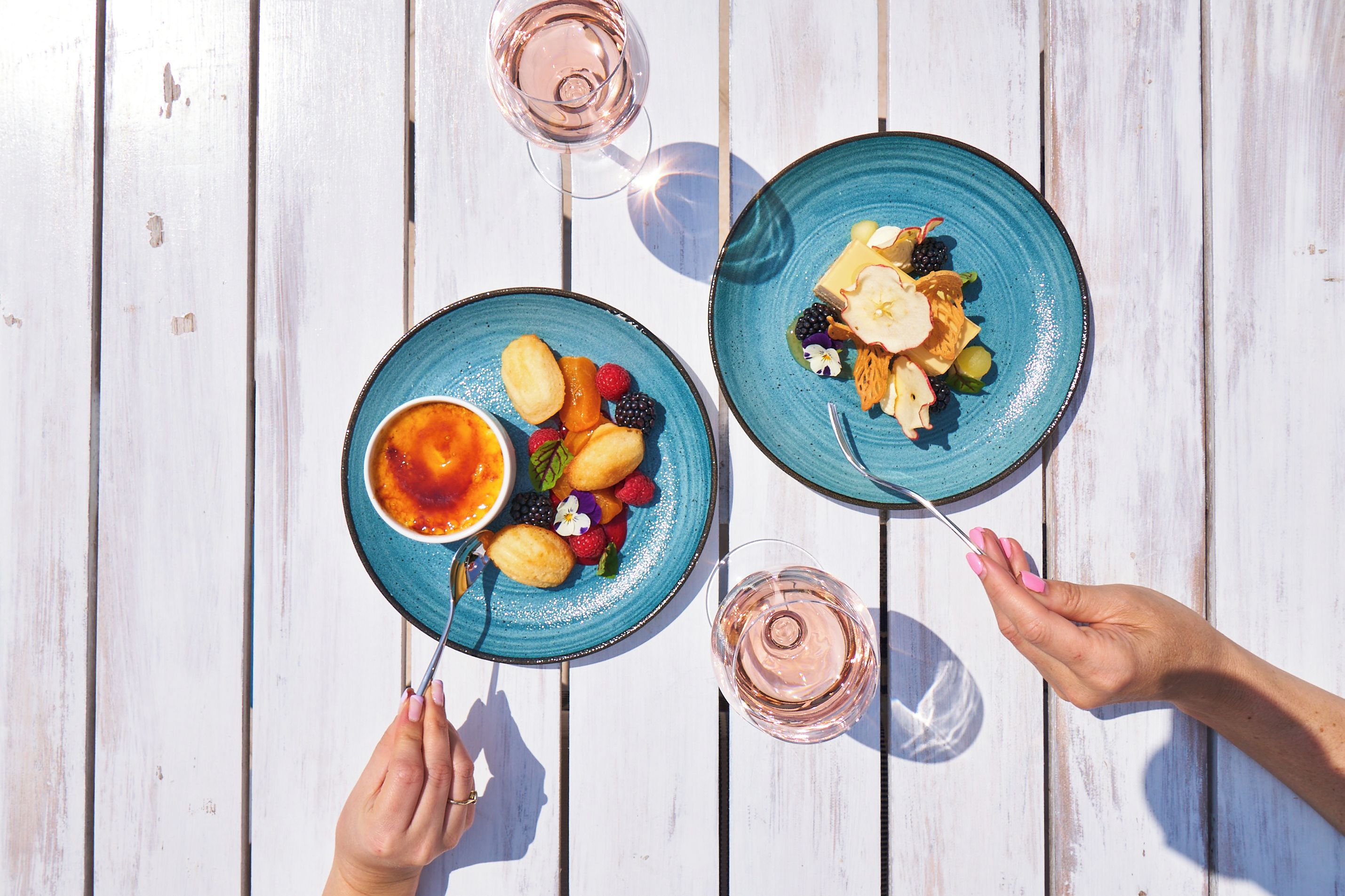 Two plates of food on a white wooden table with a glass of drink.
