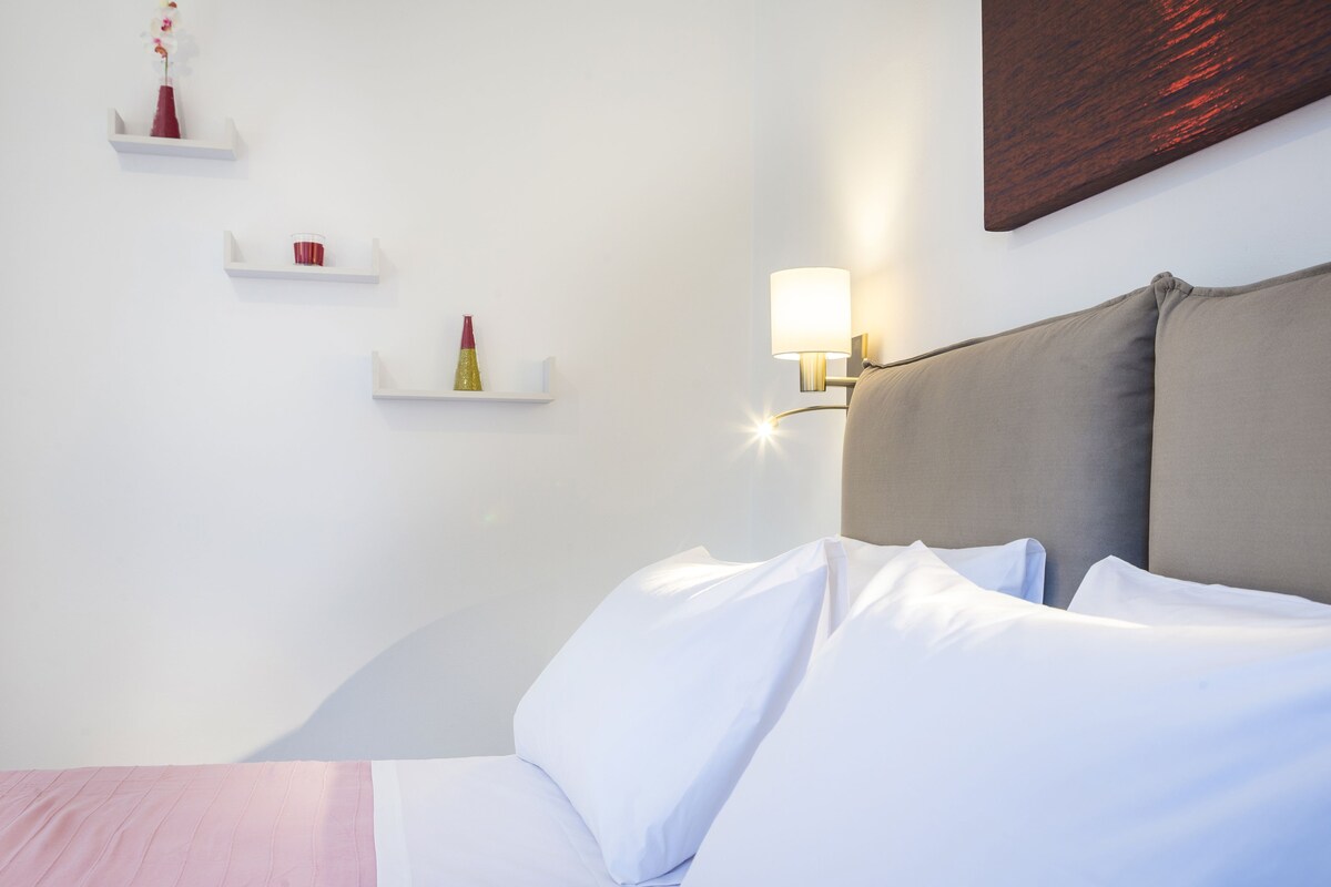 Une chambre d’hôtel bien rang ée, avec un lit, des murs blancs et une lampe fixée au mur.
