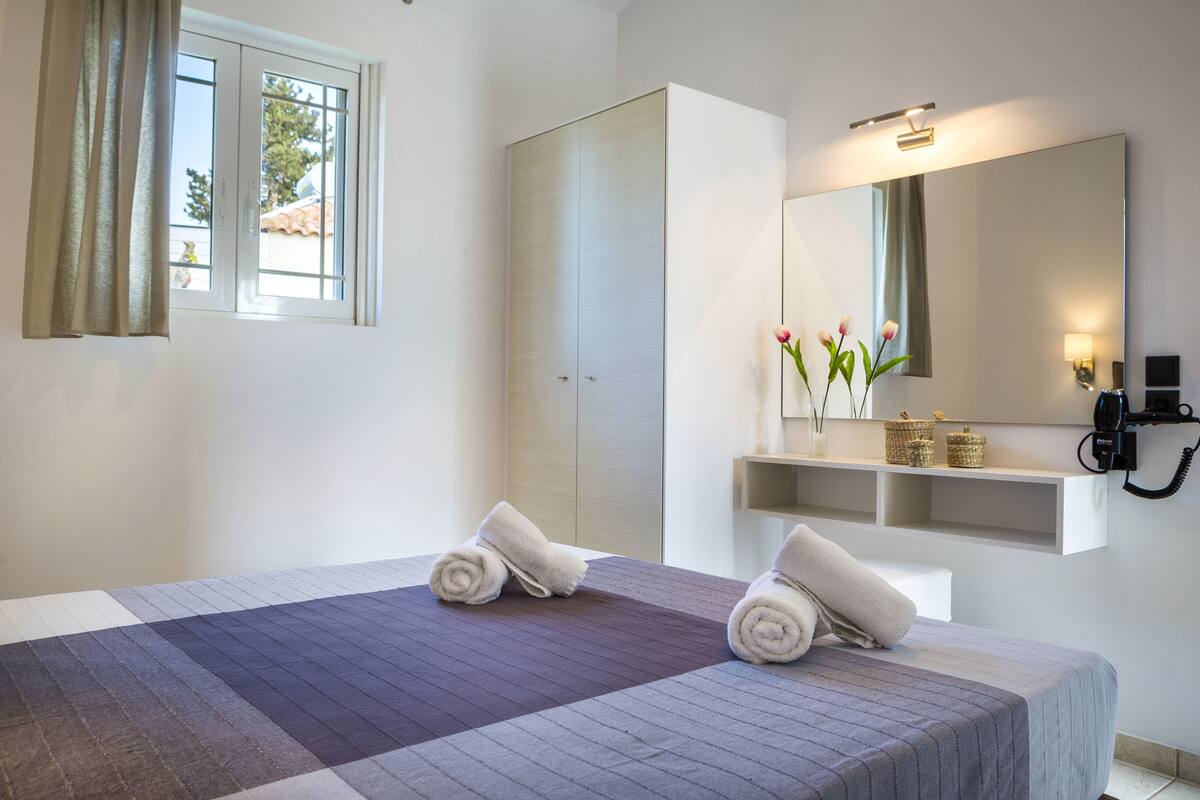 Une chambre d’hôtel avec un lit, un grand miroir, un téléphone et une fenêtre avec des rideaux.