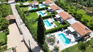 Un quartier résidentiel composé de plusieurs maisons, chacune dotée d’une piscine, et entouré de jardins bien entretenus et de grands arbres.