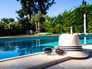 Une scène au bord de la piscine, avec un chapeau et des lunettes de soleil posés sur un rebord en pierre.