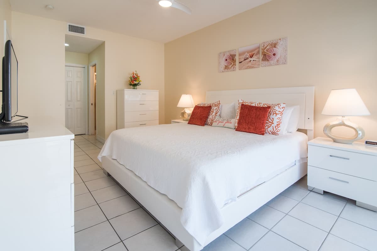 A neatly arranged bedroom with a large bed, two bedside tables with lamps, a dresser, and a television on a stand.