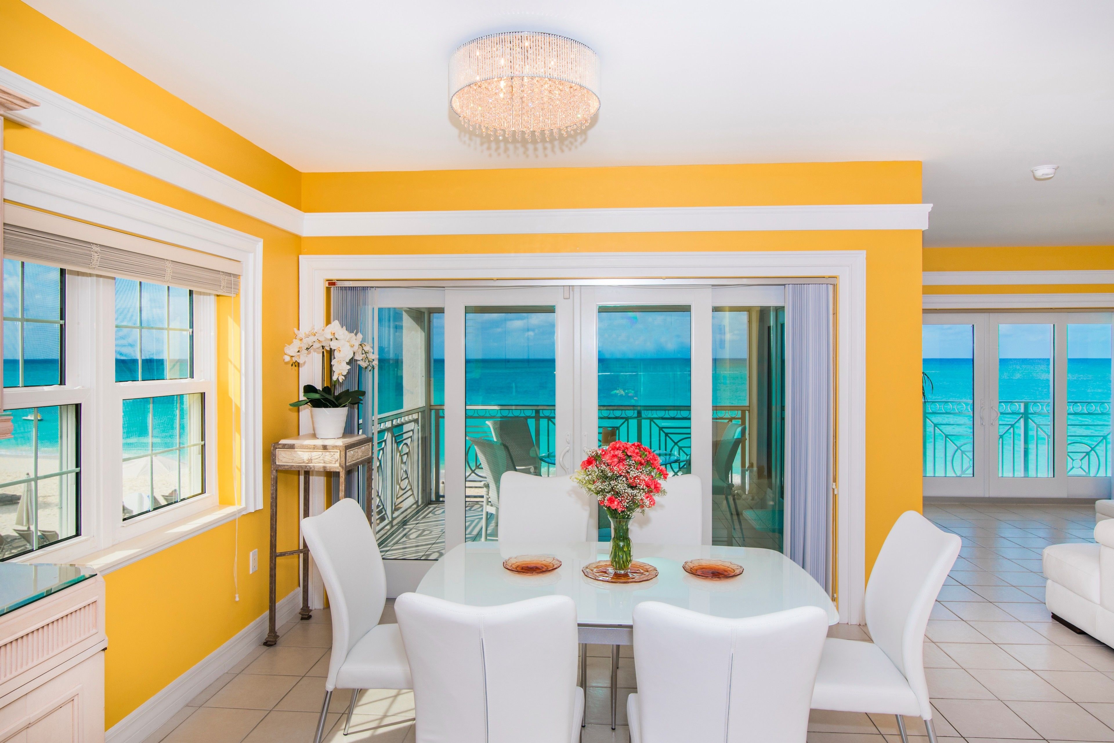 A bright yellow and white room with a glass door leading to a balcony with a view of the ocean.