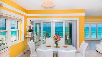 A bright yellow and white room with a glass door leading to a balcony with a view of the ocean.