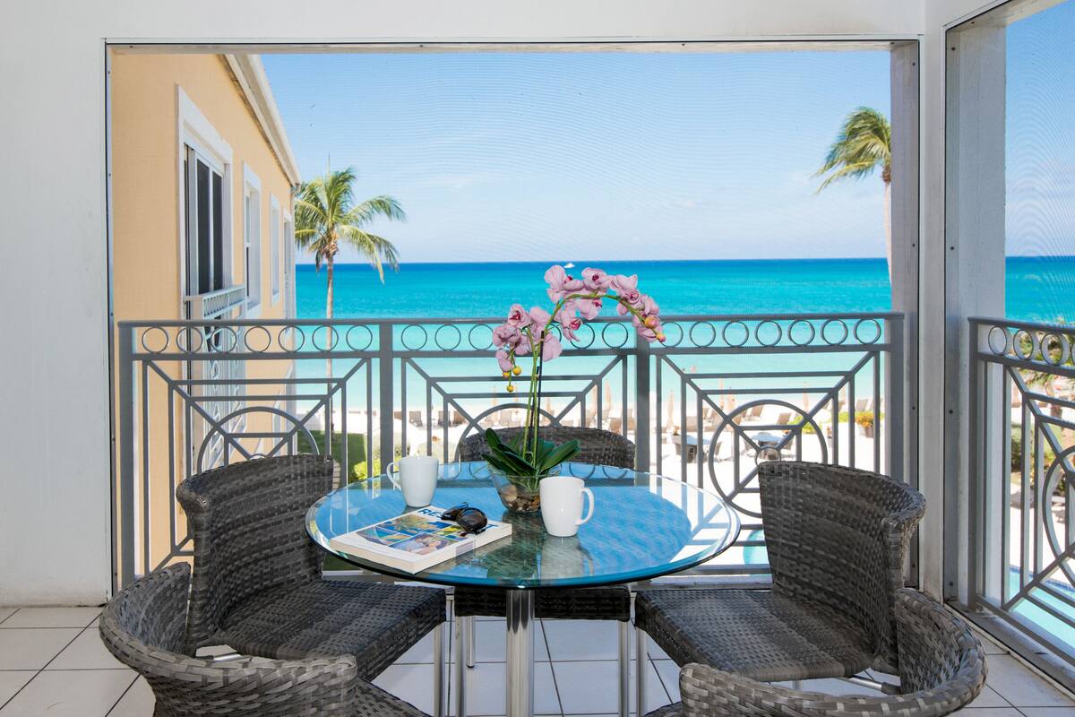 A balcony with wicker chairs, a glass table, and a view of the ocean.