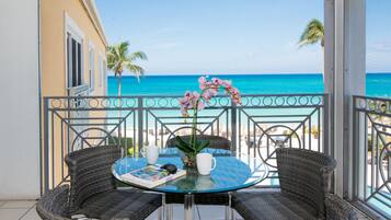 A balcony with wicker chairs, a glass table, and a view of the ocean.