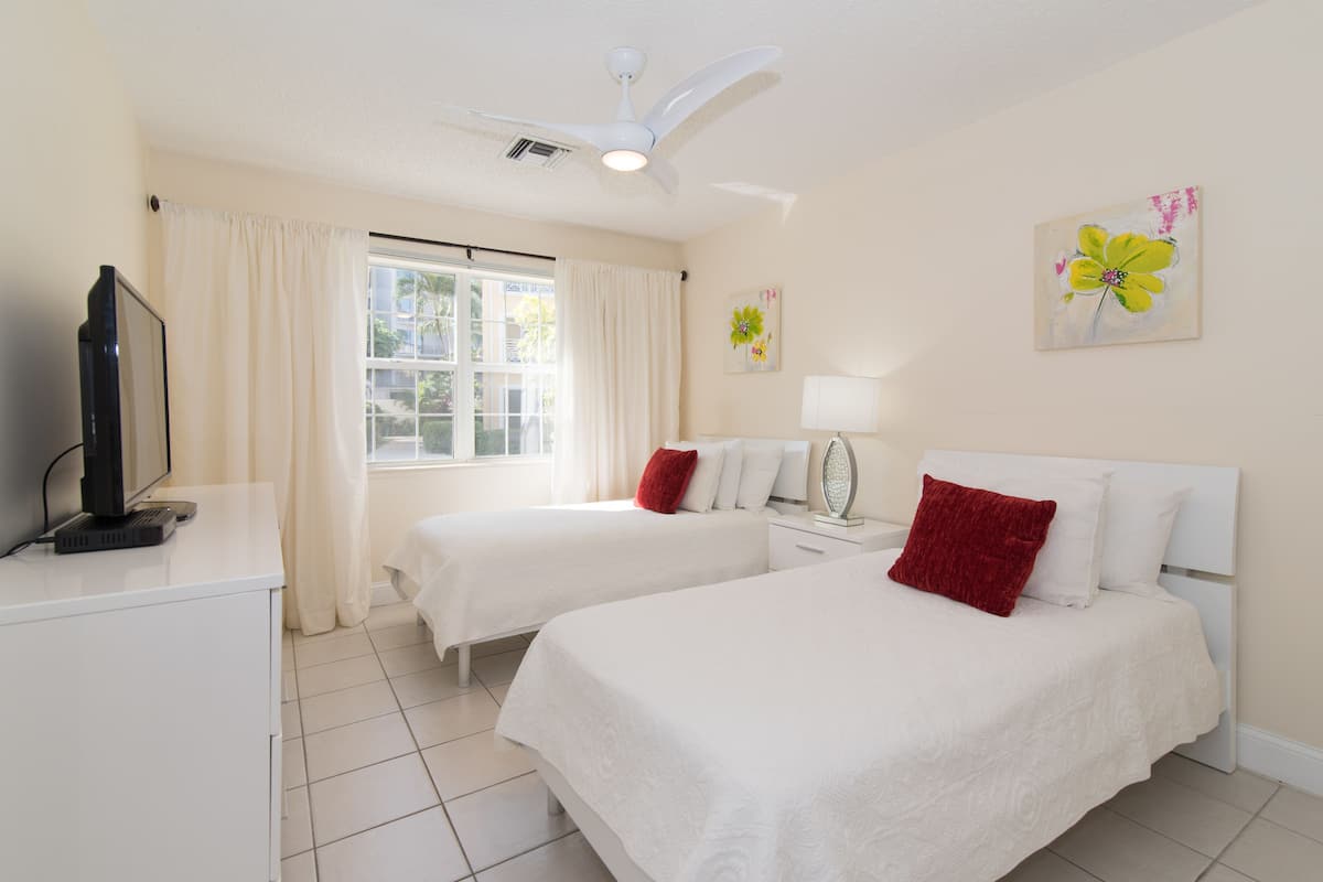 A hotel room with two beds, a TV, a ceiling fan, and a window with curtains.