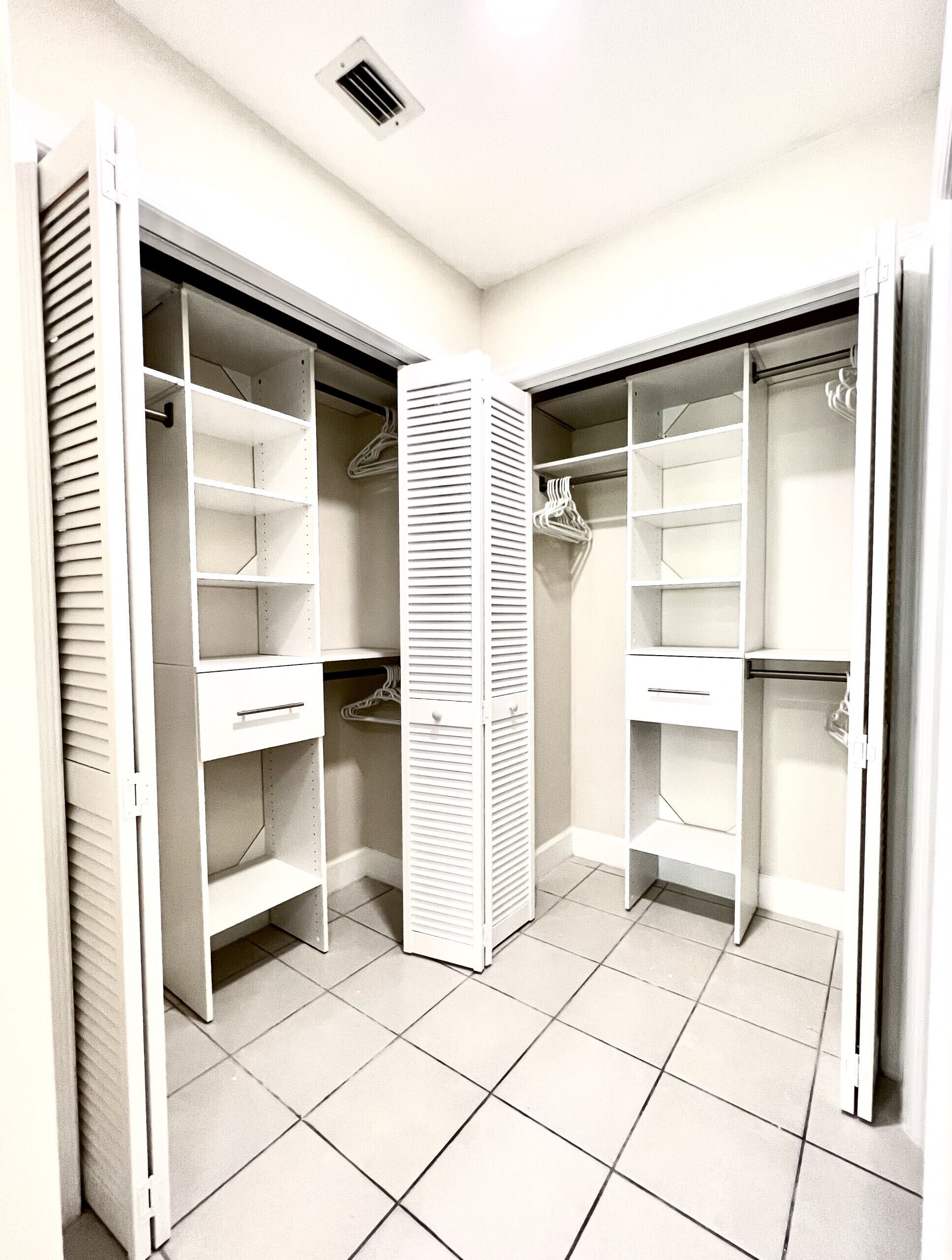 Un dressing accessible sans porte, doté de nombreuses étagères et d’espaces pour suspendre les vêtements, et dont le sol est carrelé.