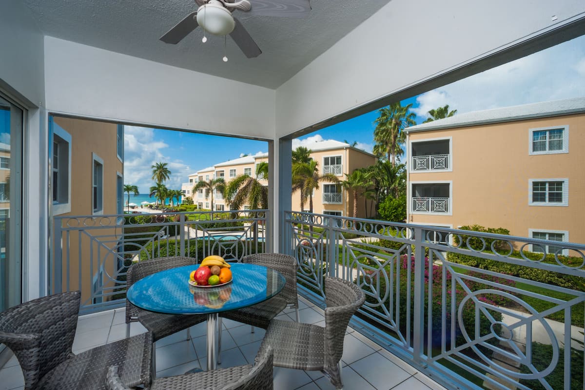 A balcony with a table and chairs, a view of a building, and a ceiling fan.