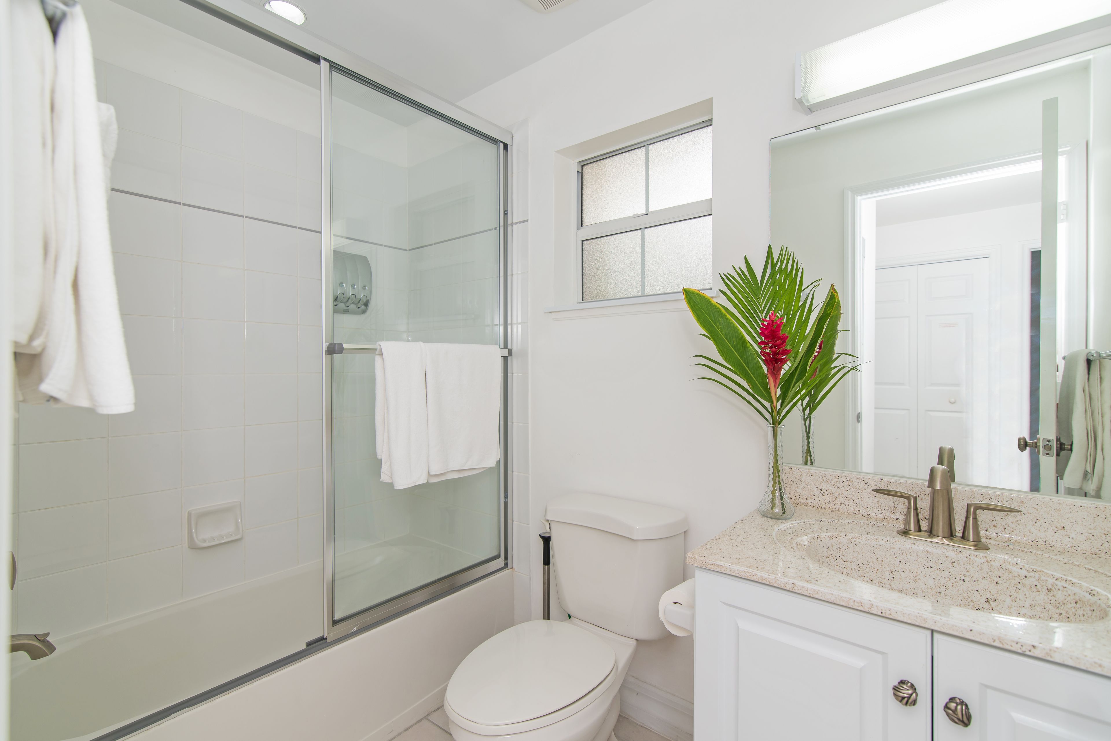 A modern bathroom with a glass shower enclosure, a toilet, a sink with a mirror, and a small window.
