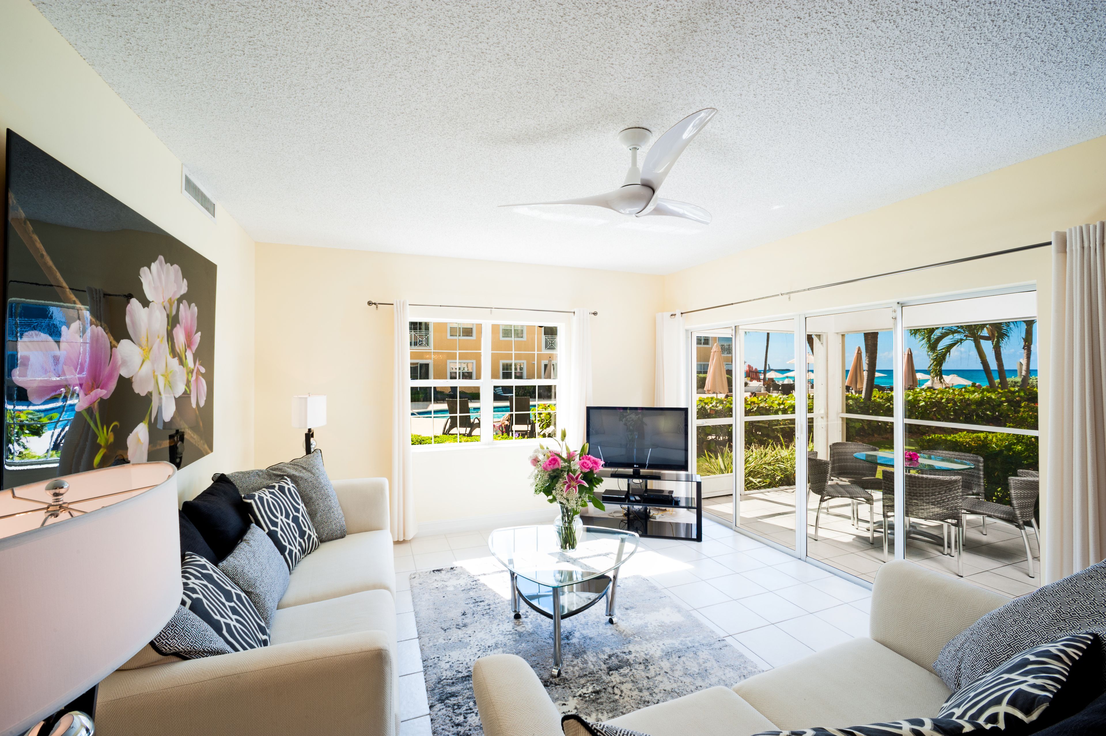 A modern living room with a sofa, coffee table, TV, and large windows offering a view of a pool and buildings.
