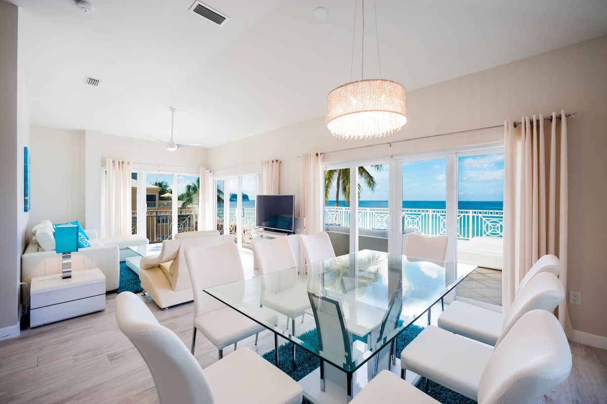 A modern living room with a glass dining table, white sofas, and a large TV.