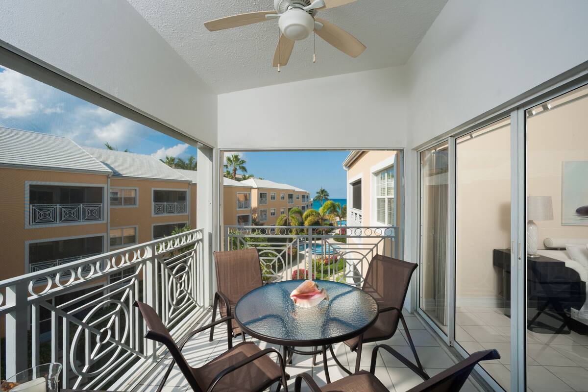 A balcony with a table and chairs, a ceiling fan, and a view of other buildings and palm trees.