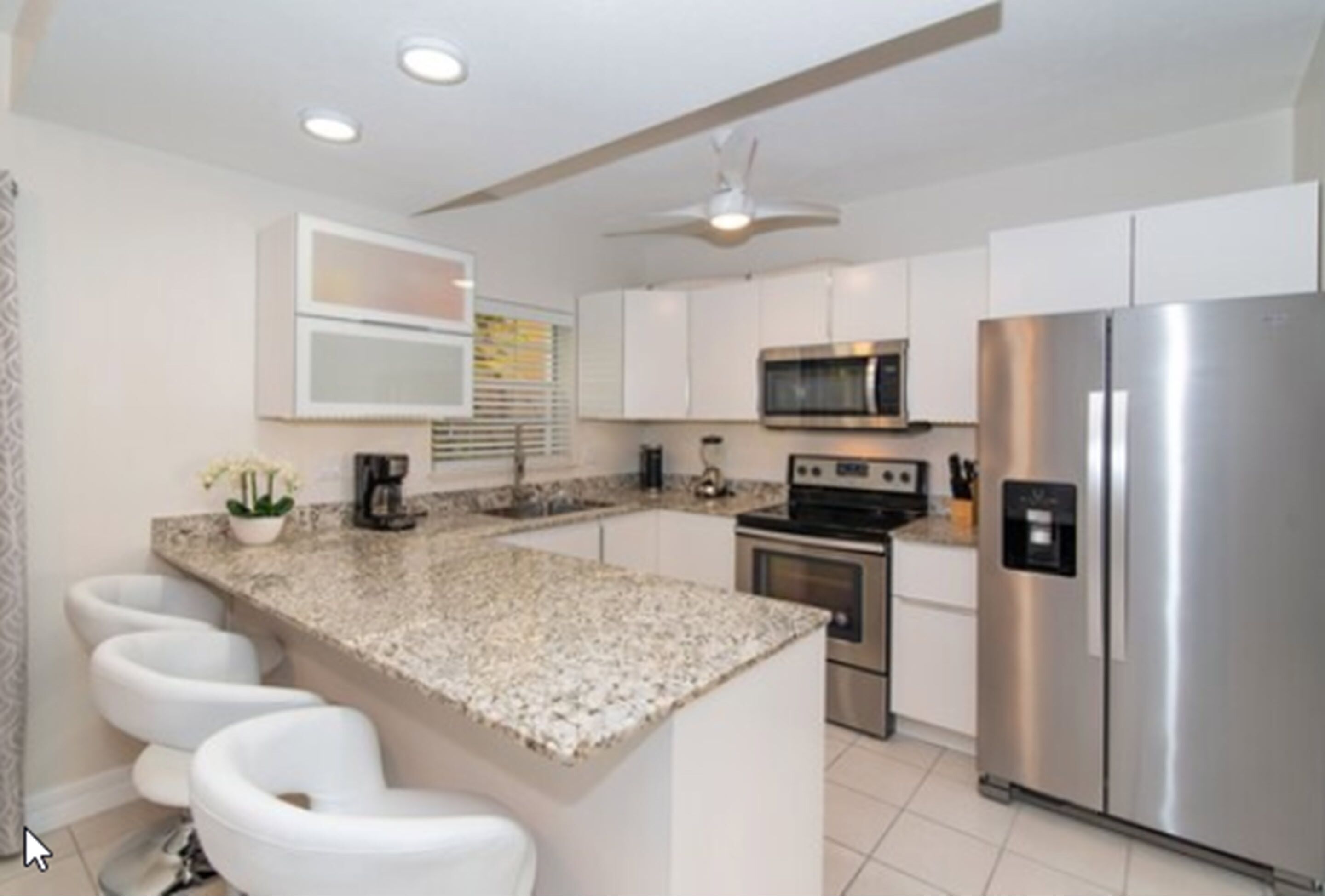 A modern kitchen with white cabinets, a granite countertop, a stainless steel refrigerator, and a built-in oven.