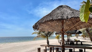 Une plage avec un parasol en chaume et des tables en bois.