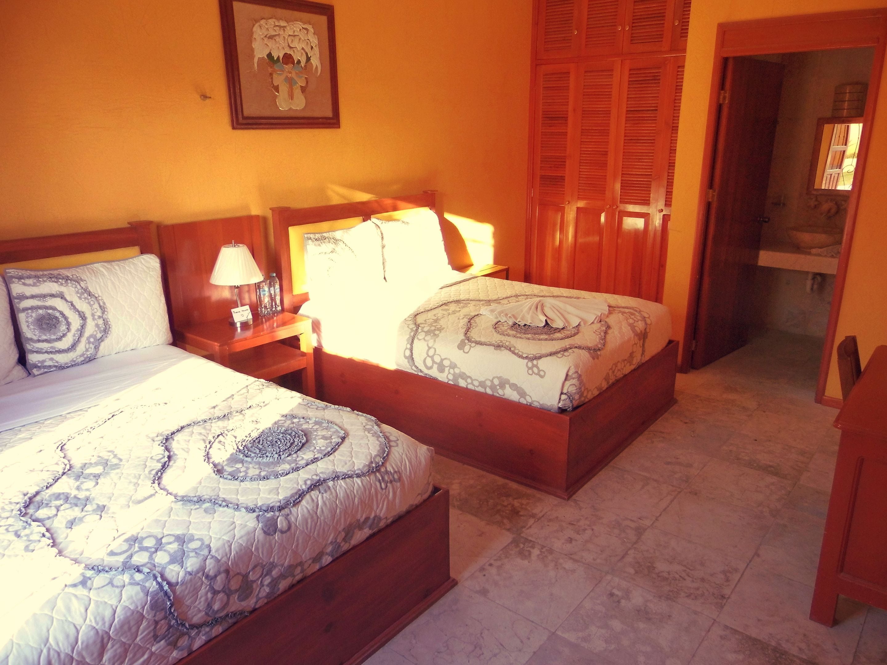 A hotel room with two beds, wooden headboards, a nightstand with a lamp, and a framed picture on the wall.