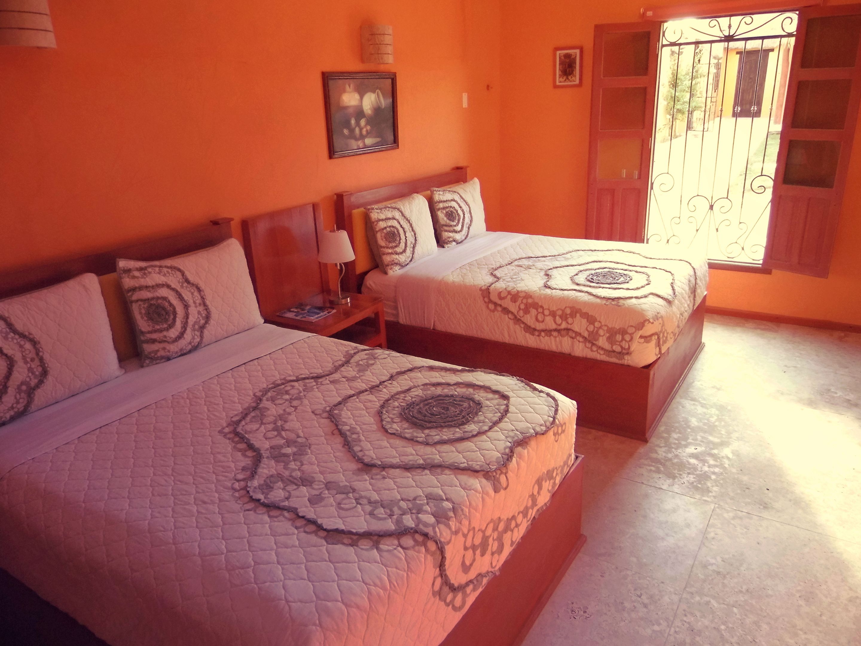 Una habitación con dos camas, cada una con ropa de cama y almohadas estampadas. Hay una mesita de noche con una lámpara y un cuadro en la pared.