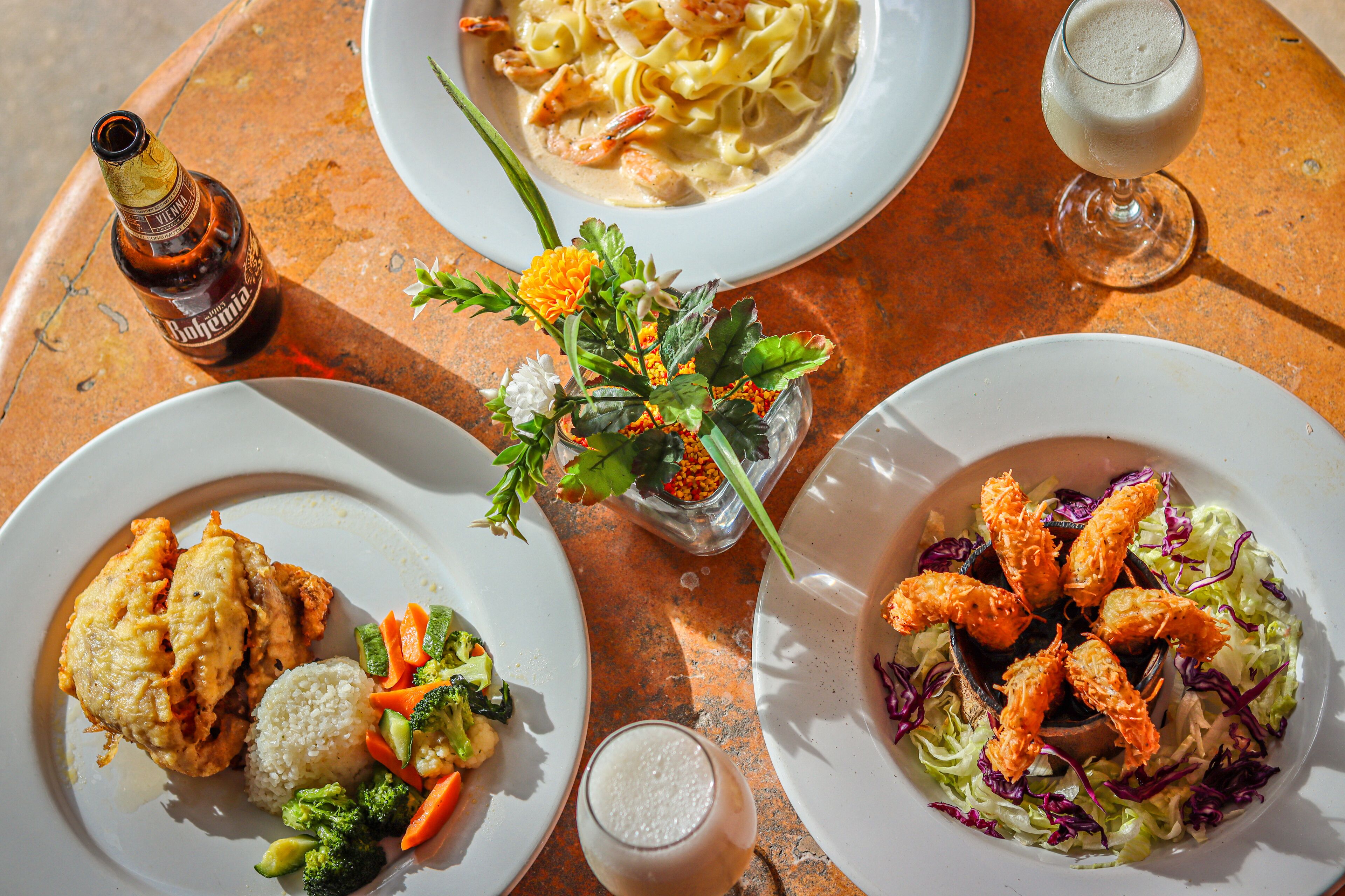 A table with three plates of food, a bottle, and a glass of beer.