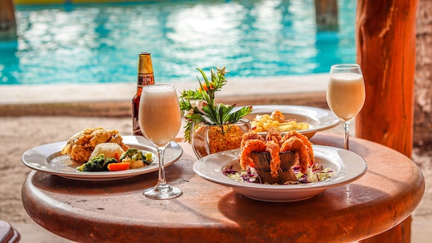 Une table à manger dressée avec des plats de fruits de mer, des boissons, et une vue sur une piscine.