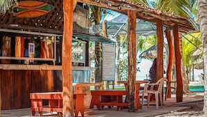 Un espace extérieur aménagé en bois, avec des bancs et des tables, entouré de palmiers et offrant une vue sur l’océan.