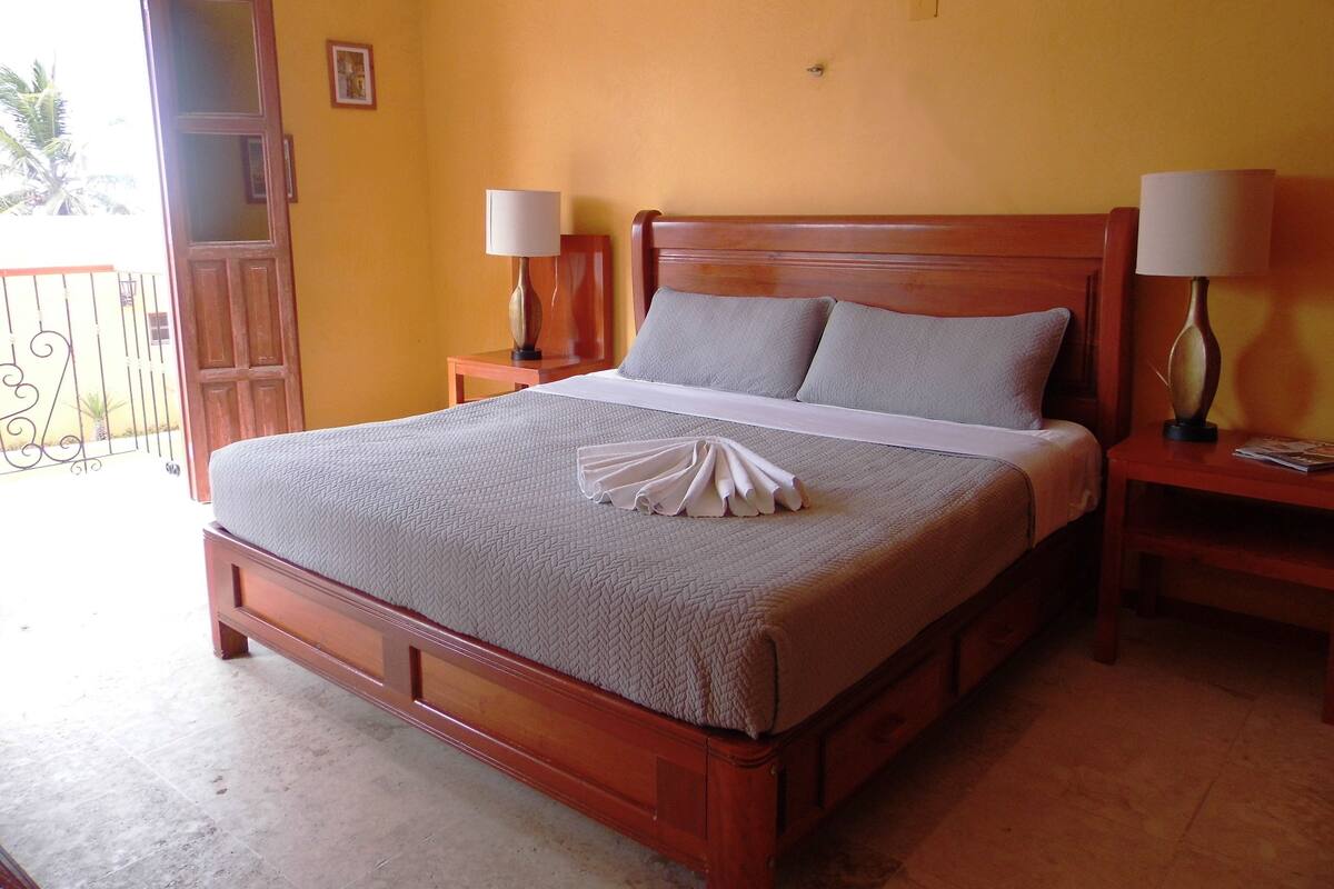 A neatly made bed with a folded towel, wooden headboard, two bedside lamps, and a wooden nightstand.