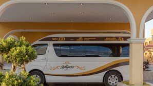 Un autobús blanco con la señalización "San Ignacio Hotel" y "Piscina", estacionado bajo una estructura en arco.