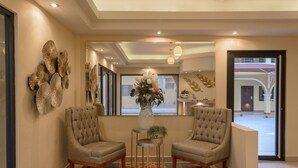 Un pasillo bien iluminado con dos sillones tapizados, un jarrón decorativo con flores y una alfombra estampada.
