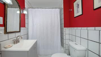 Casa de banho com sanita branca, lavatório com saboneteira, cortina de chuveiro e espelho.