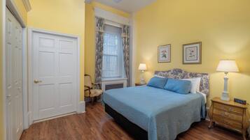 A bedroom with a bed, two bedside tables, a window with curtains, a ceiling fan, and a door.