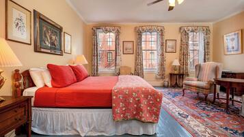 A bedroom with a bed, a chair, a desk, a ceiling fan, and two windows with curtains.