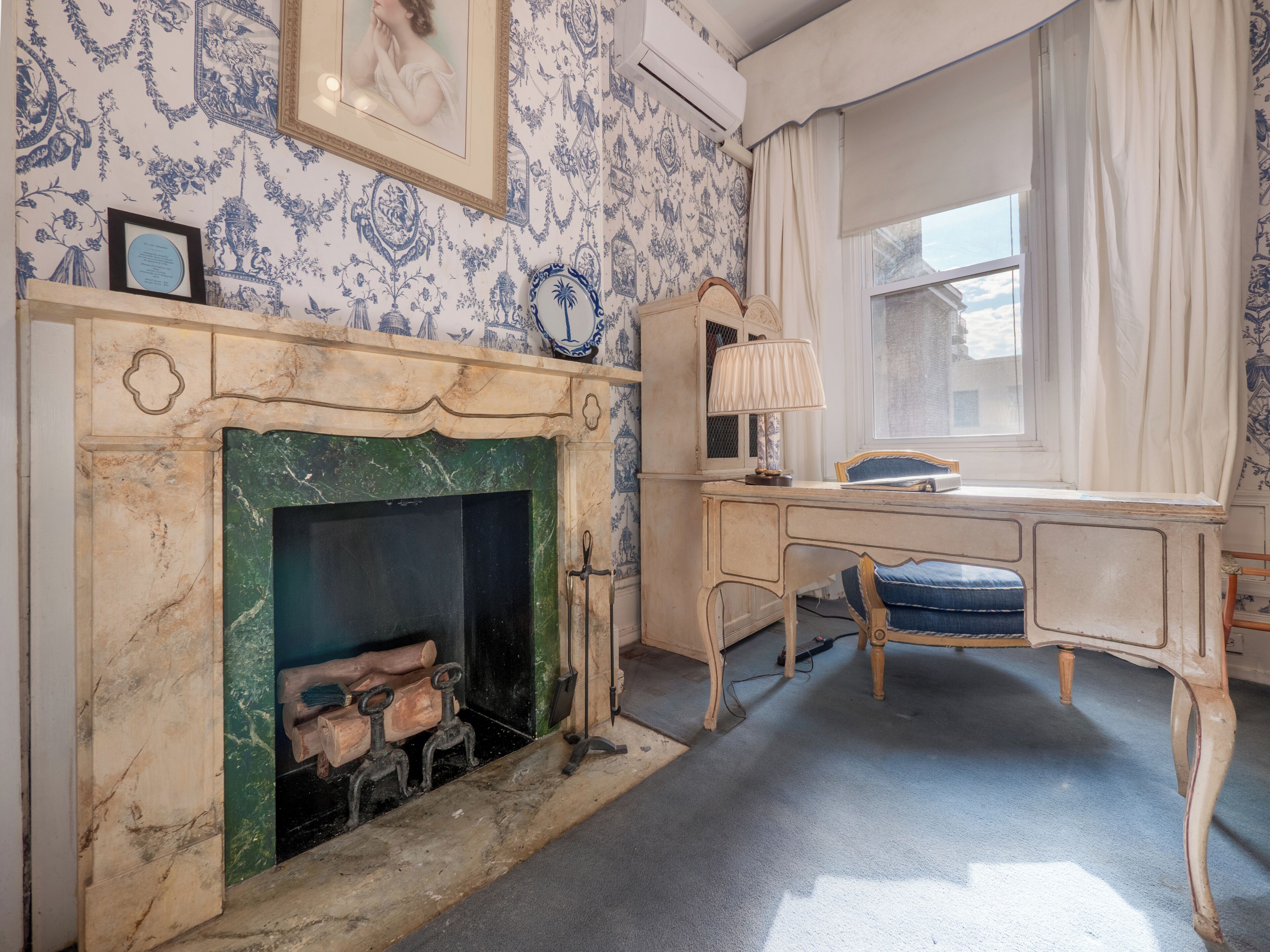 Une pièce avec une cheminée, un bureau, une chaise et une fenêtre avec des rideaux.
