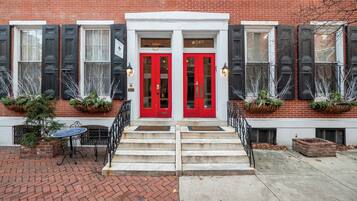 A red double door entrance with a brick facade, steps leading up to it, and two potted plants on either side.