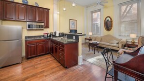 A kitchen with wooden cabinets, a refrigerator, and a microwave. There is a dining area with a sofa and a table. - La Reserve on Pine (Philadelphia)