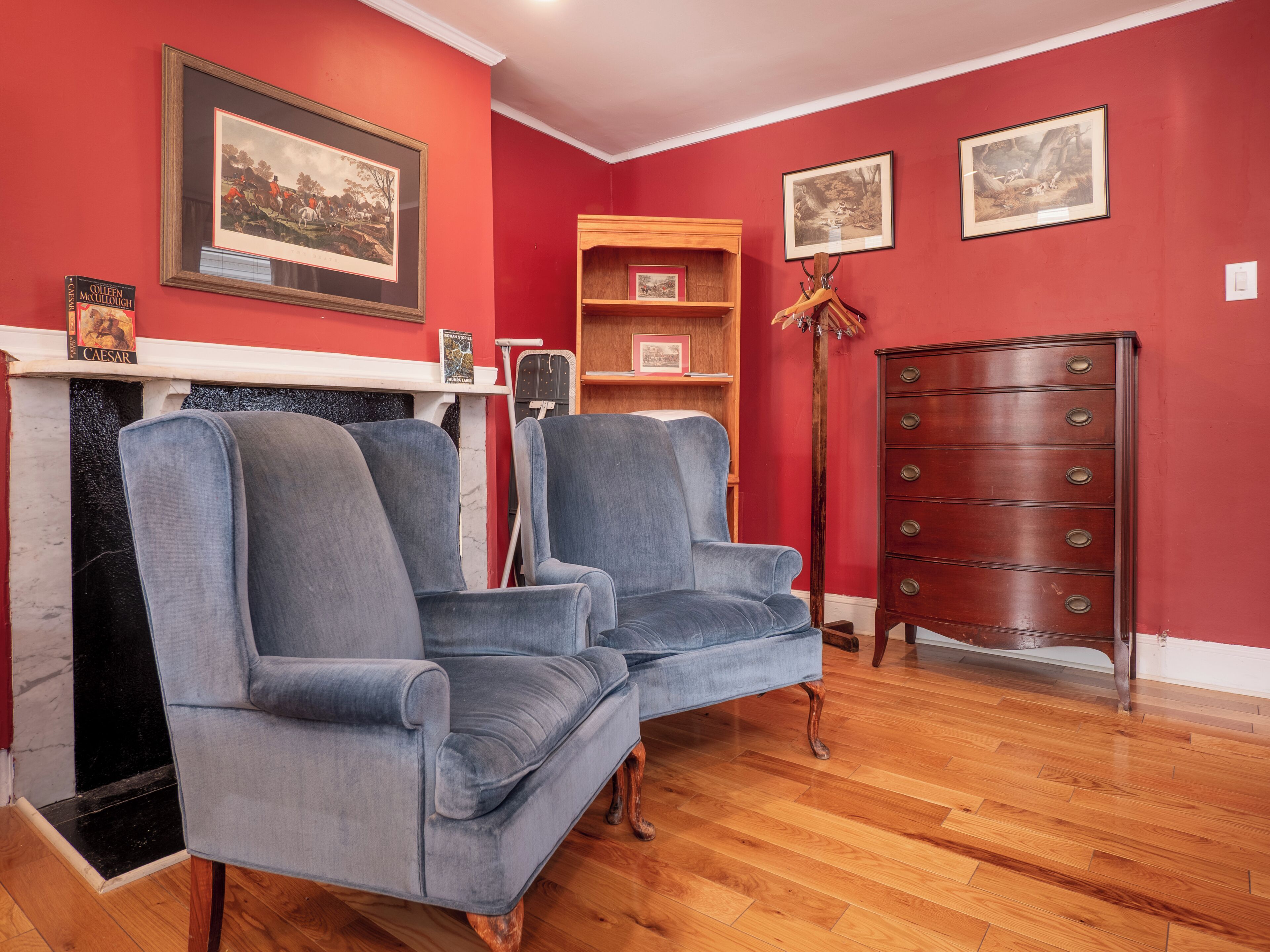 A room with a fireplace, two armchairs, a wooden dresser, and a bookshelf.