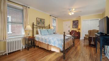 A bedroom with a bed, a ceiling fan, a radiator, a television, and a chair.