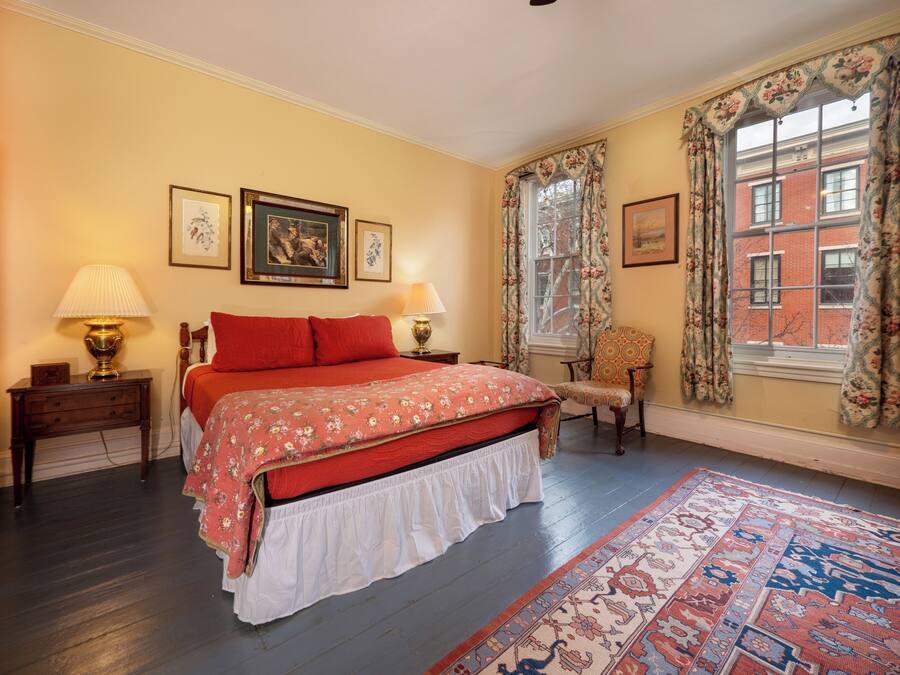 Una camera con un letto, due lampade da comodino, una poltrona, una finestra con tende floreali e un tappeto decorato.