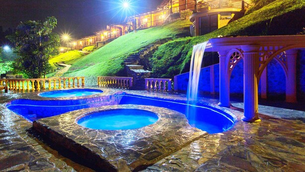 A nighttime view of a hotel with a pool area, a waterfall, and a staircase leading up a hill. - Finca Hotel Rancho San Antonio (Salento)