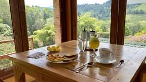 A wooden table with breakfast items, a glass of water, a glass of juice, and a cup with a saucer. - Finca Hotel Rancho San Antonio (Salento)
