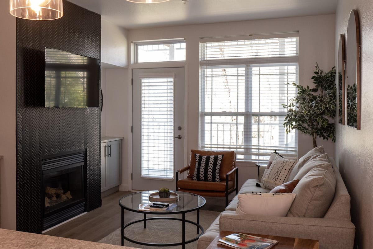 A living room with a fireplace, a sofa, a coffee table, and large windows with blinds.