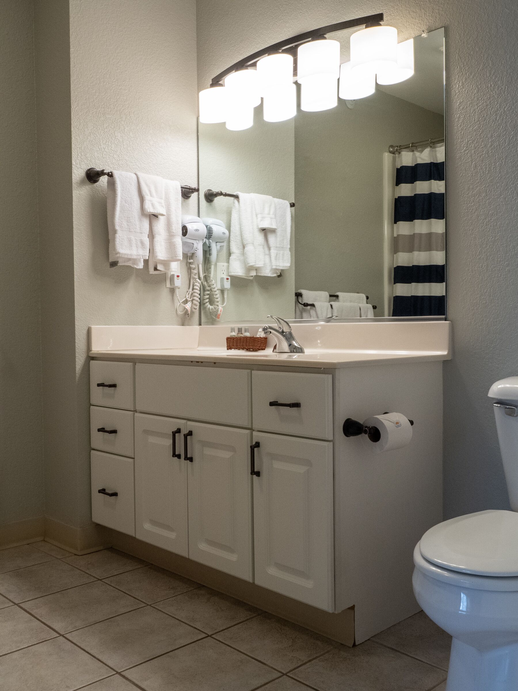 A bathroom with a white sink, a mirror, a towel rack, a toilet, and a roll of toilet paper.
