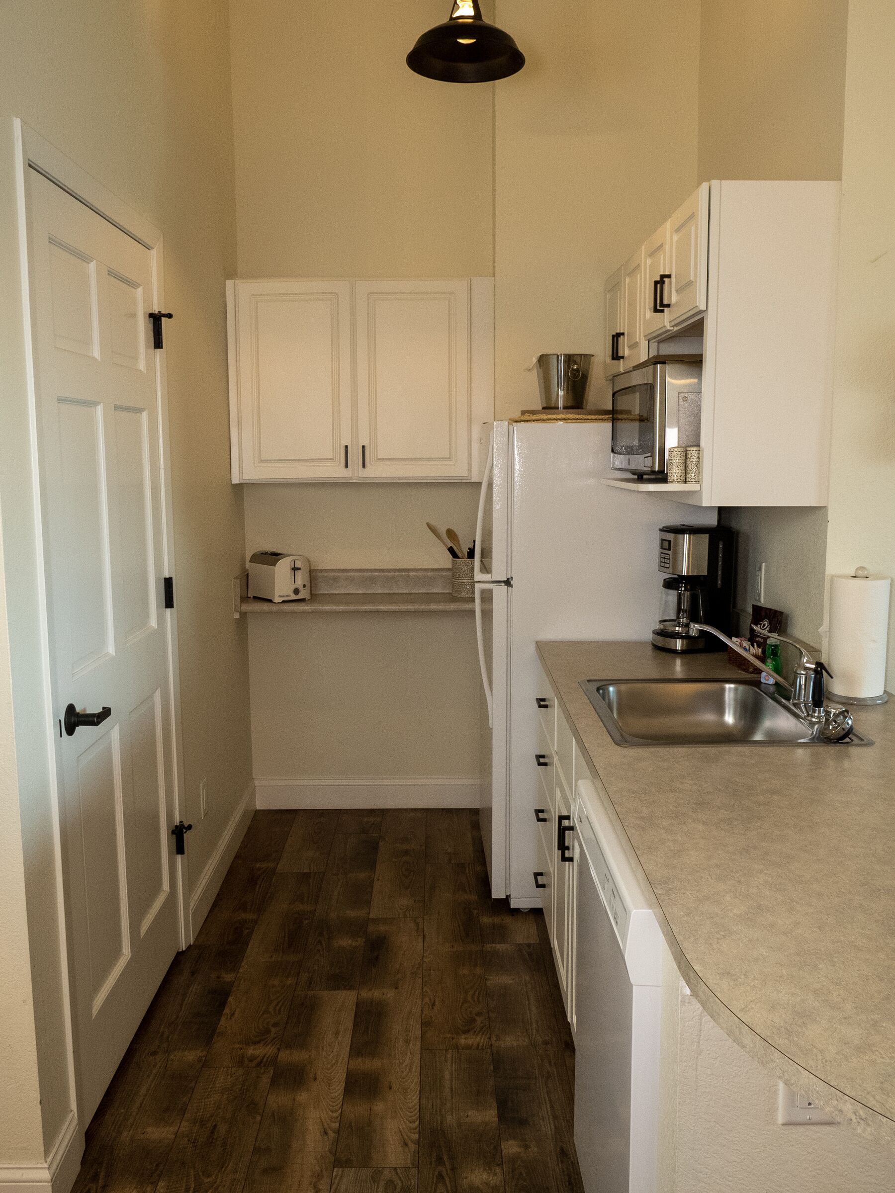 A compact kitchen with white cabinets, a stainless steel sink, and a microwave.